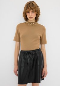 Béžový top s krátkým rukávem, texturovaný, zdobený kamínky kolem límečku, kombinovaný s černou sukní z umělé kůže s elastickým pasem.