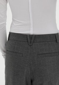 Grijze broek met een dunne streep, voorzien van twee achterzakken, een platte tailleband en een subtiele textuur. Gemaakt met een wit langslaven top.