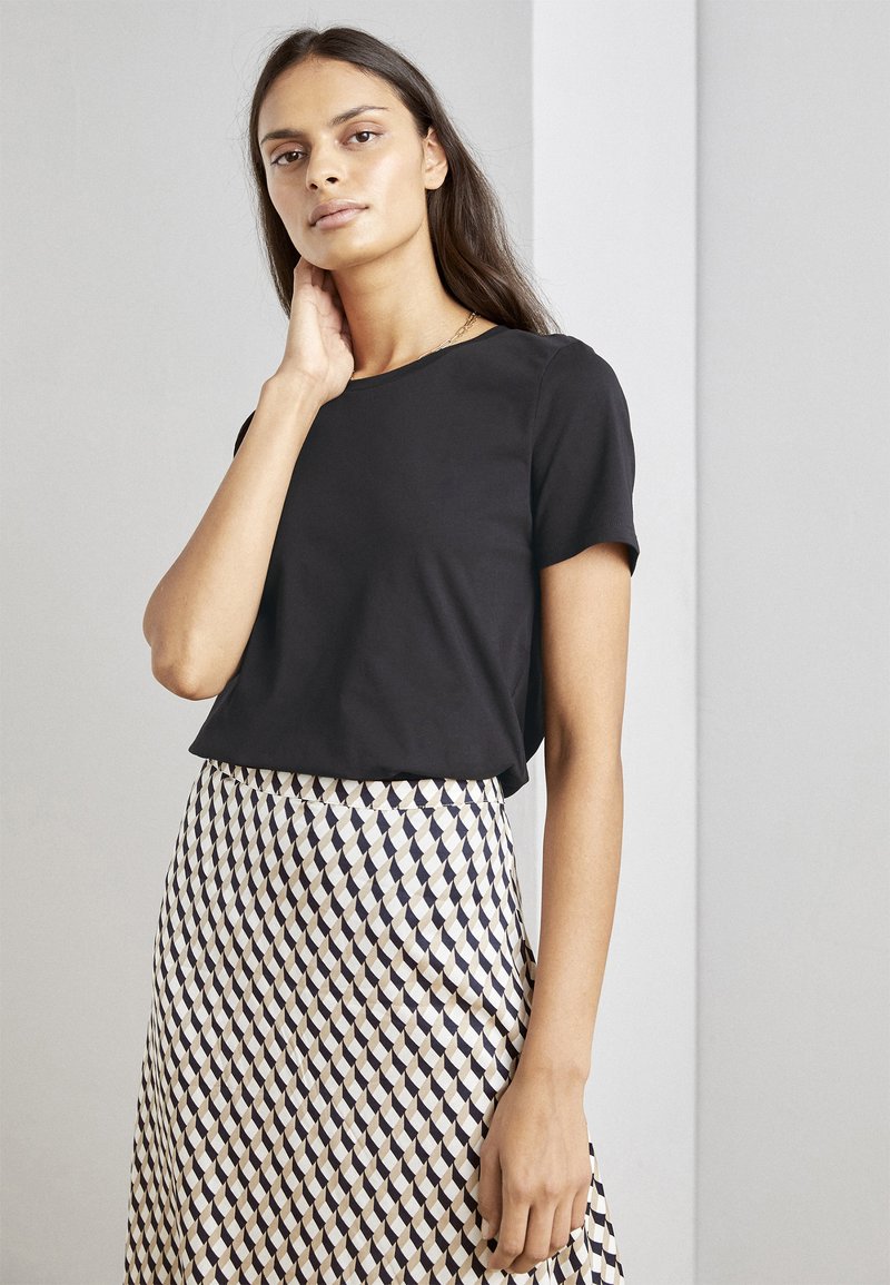 Zwarte T-shirt met korte mouwen, gecombineerd met een gebloemd rokje met crèmekleurige, marineblauwe en donkerbruine geometrische vormen. Glad textuur van de stof.