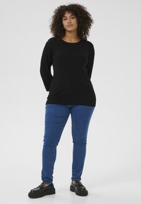 Top de manga larga negro con canalé y escote redondo, combinado con jeans ajustados azules y zapatos de plataforma negros. Fondo blanco liso.