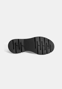 Zwarte rubberen schoenzool met een gestructureerd, geribbeld patroon en diepe groeven voor grip. Ronde neus en platte hak voor stabiliteit.