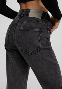 Svarta denimjeans med hög midja, försedda med en läderlapp bak och två traditionella bakfickor, som har en blekt textur.