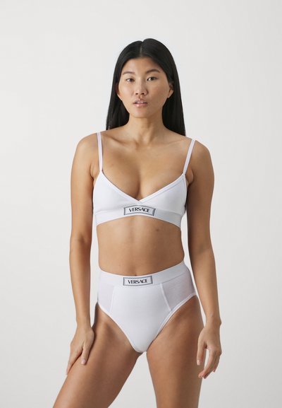Valge puuvillane bralette ja kõrge vöökohaga aluspesu komplekt, millel on v-kaeluse disain ja kontrastne logo vöö. Libe tekstuur, lihtne stiil.
