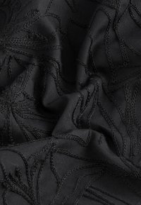 Schwarzer Stoff mit kunstvollen, bestickten Blattmustern. Texturierte Oberfläche mit einem weichen Fall und sichtbaren Stickdetails.