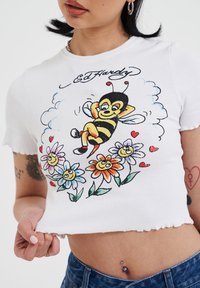 Witte cropped t-shirt met een kleurrafische afbeelding van een ontspannen bij omringd door glimlachende bloemen, met een gescheurde zoom en geribbelde textuur.
