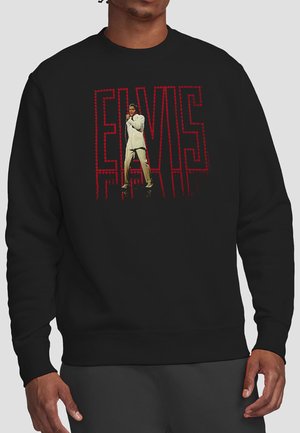 Man wearing black sweatshirt with red "ELVIS" text and image of Elvis Presley in white suit singing on front.