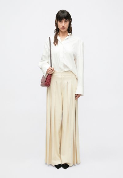 Cămașă albă cu mâneci lungi, pantaloni largi crem cu pliuri și geantă crossbody vișinie. Material texturat, linii elegante și croială ajustată.