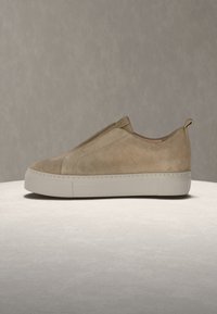 Παιδί παπούτσι τύπου slip-on από σουέντ σε καφέ απόχρωση με παχιά λευκή σόλα και κορδόνι τράβηγμα, εμφανίζεται σε πλευρικό προφίλ σε ουδέτερη επιφάνεια και φόντο.