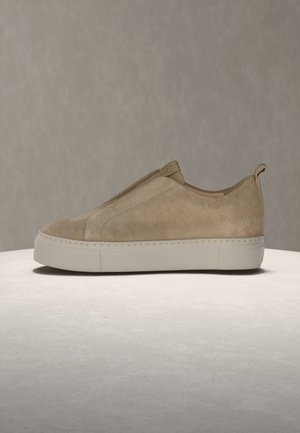 Beżowy zamszowy tenisówka wsuwana z białą grubą podeszwą i pętelką do zakładania, widoczna z boku na neutralnym tle i powierzchni.