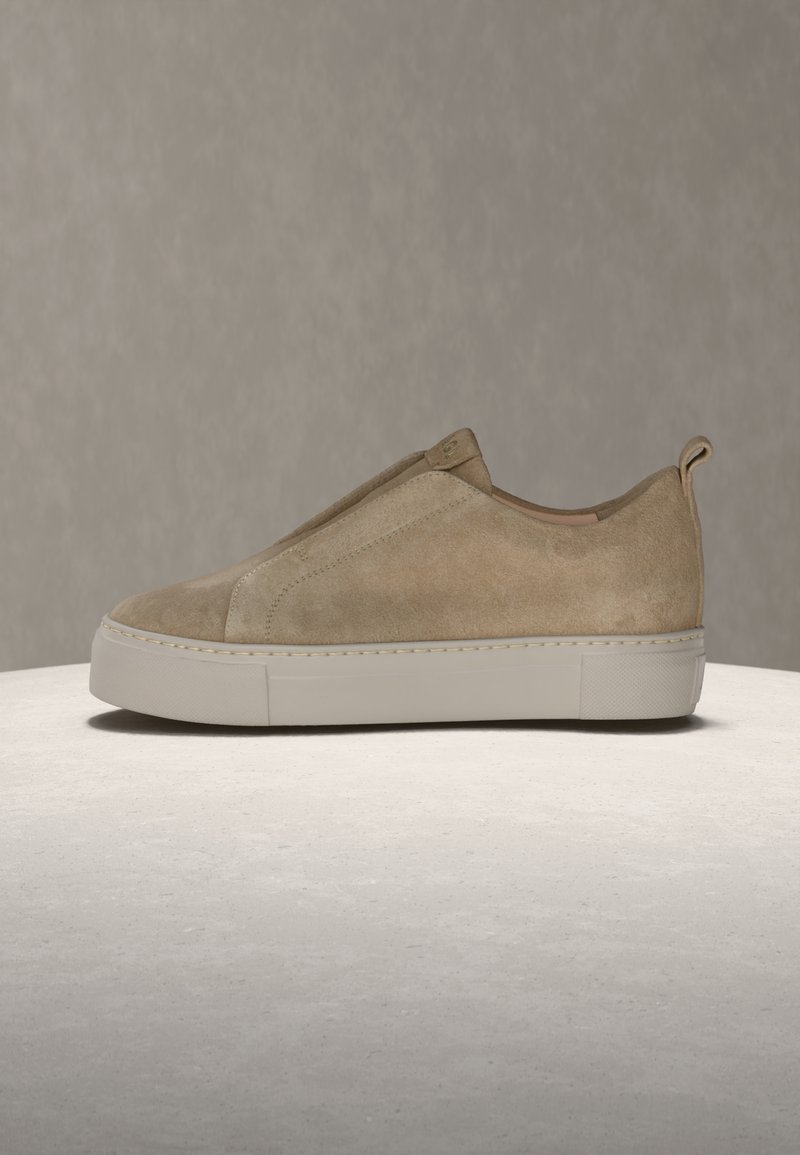 Παιδί παπούτσι τύπου slip-on από σουέντ σε καφέ απόχρωση με παχιά λευκή σόλα και κορδόνι τράβηγμα, εμφανίζεται σε πλευρικό προφίλ σε ουδέτερη επιφάνεια και φόντο.