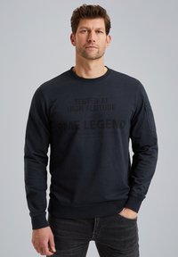 Granatowy sweter z okrągłym dekoltem, z dużym nadrukiem graficznym w czarnym kolorze z przodu oraz kieszenią naszywaną na rękawie.