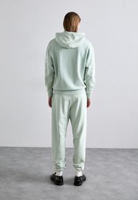 Lyse mintgrøn sweatsuit bestående af en hætte sweatshirt og matchende joggingbukser, fremstillet af blødt stof med ribbede manchetter og en afslappet pasform.