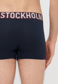 Sötétkék boxer alsó maroon színű rugalmas derékkal, amelyen „STOCKHOLM” felirat található szürke betűkkel. Puha anyag, amely jól illeszkedik.