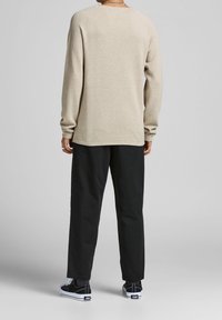 Beiger Strickpullover mit lässiger Passform, langen Ärmeln und gerippten Bündchen, kombiniert mit schwarzen Hosen und schwarzen Sneakern mit weißen Sohlen.