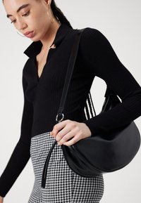 Zwarte leren schoudertas met een gebogen vorm en een gladde textuur, voorzien van een lange band en een zilveren hardwareaccent.