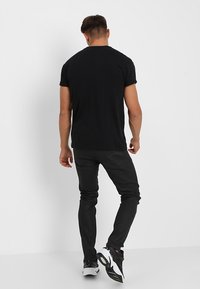 Svart bomull T-shirt med korta ärmar och rundad halsringning, tillsammans med mörka jeans. Outfitten kompletteras av vita och svarta sneakers.