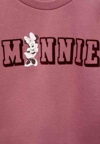 Sweat-shirt rose avec le grand lettrage « MINNIE » en rouge foncé, accompagné d'un graphique d'un personnage de dessin animé portant une robe et un nœud sur le côté gauche.