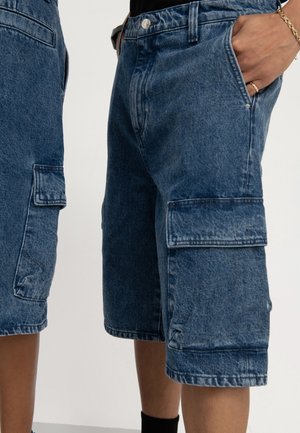 Spodnie szorty cargo z denimu w średnim odcieniu niebieskiego, z wieloma kieszeniami, luźnym krojem i prostą nogawką wykończoną postrzępionym brzegiem.