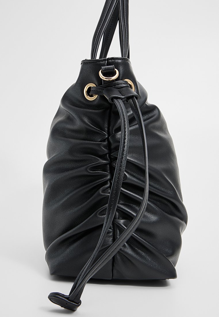 Bolso de tiro de cuero negro con textura fruncida, acentos de hardware dorado y dos correas para los hombros. Superficie suave y lisa.