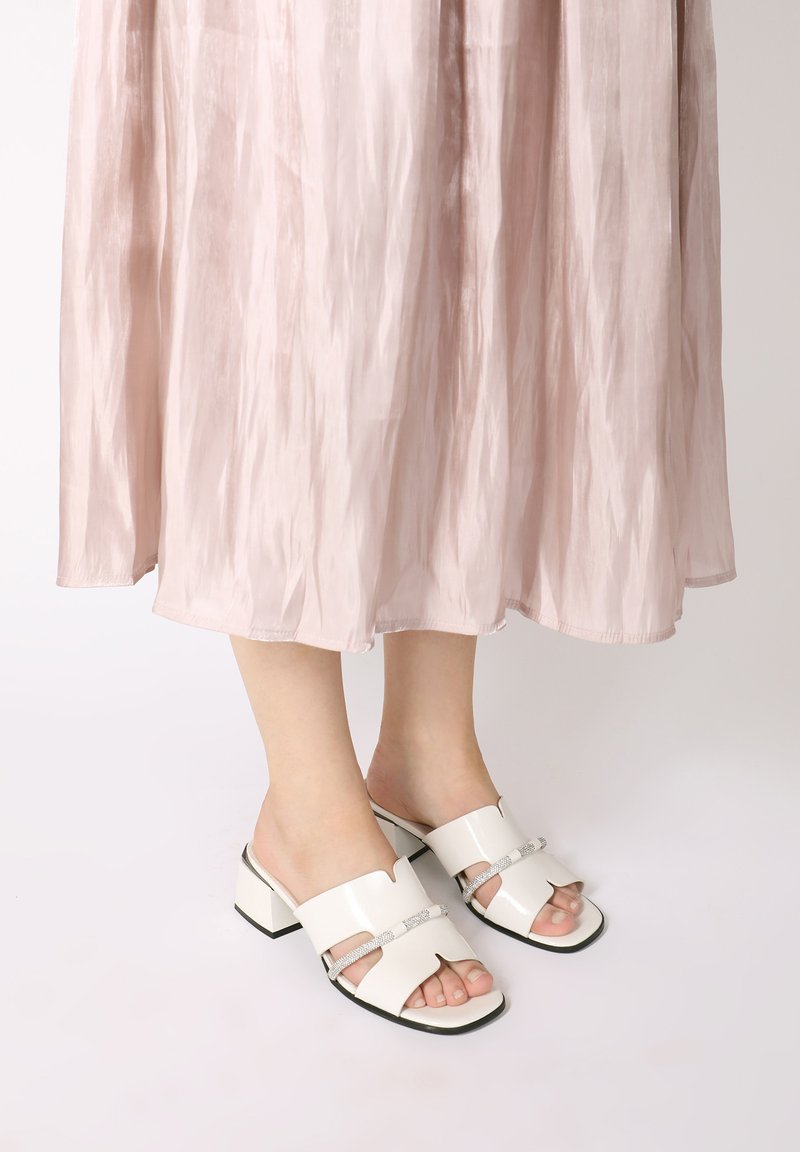 Witte gepatenteerde leren blokhak mules met twee uitgesneden banden en metallic accentdetails. Gladde oppervlakte met een glanzende afwerking.