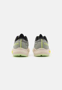 Des chaussures de course avec une tige en tissu gris et des accents noirs, une semelle beige clair et des touches de jaune fluo. Le design comprend des motifs texturés.
