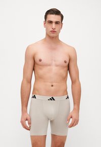 Boxer briefs bege com um cós listrado em preto, feitos de um tecido suave. O ajuste é justo ao corpo, com uma textura suave e um design elástico.