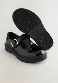 Chaussures en cuir verni noir avec une sangle à boucle, bout rond, semelle épaisse en caoutchouc noir avec un motif d'étoiles et finition lisse.