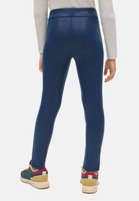 Leggings azul marino con textura suave, cintura alta y diseño ajustado. Combinados con zapatillas deportivas multicolores.