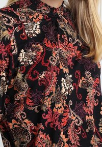 Top in tessuto nero con vivaci motivi floreali a paisley in rosso, arancione e crema. Collo arr gathered con finitura testurizzata.
