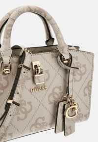 Borsa beige in tela testurizzata, con hardware dorato, doppio manico e un ciondolo. Presenta un motivo logo e un design strutturato.