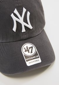 Gorra de algodón gris ajustable con logotipo bordado en blanco "NY" y una etiqueta negra con el texto "47 CLEAN UP". Tela texturizada.