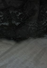 Tela de encaje negro superpuesta sobre malla negra lisa, con intrincados patrones florales y un acabado suave y texturizado. Los bordes están ligeramente deshilachados.