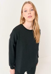 Felpa nera oversize con colletto e polsini a costine, caratterizzata da una vestibilità rilassata e una texture morbida, mostrata su un modello con capelli lunghi.