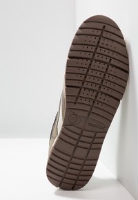 Brązowa gumowa podeszwa z teksturowanym bieżnikiem, z poziomymi liniami i otworami zapewniającymi wentylację. Na boku wytłoczona etykieta marki „Geox”.
