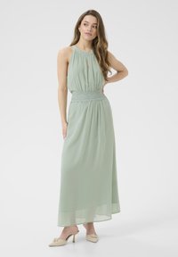 Maxi dress in soft mint green chiffon with a halter neckline and keyhole detail. Styled with a lace-accented waist and flowy silhouette.
