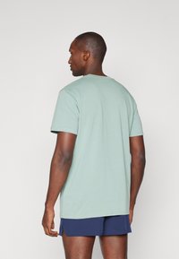 Mentazöld pamut póló kerek nyakkal, rövid ujjal és lazán illeszkedő fazonnal, navy kék rövidnadrággal párosítva. Tiszta, egyszerű dizájn.