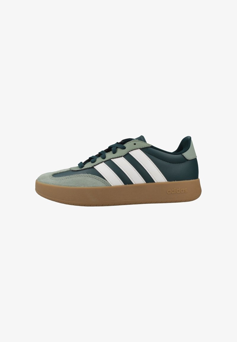 Baskets Adidas basses avec dessus vert foncé et gris clair, trois bandes blanches, semelle en caoutchouc gomme et lacets noirs.
