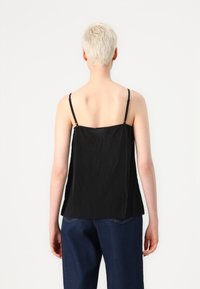 Svart ermeløs topp med plisserte detaljer, tynne justerbare stropper og løs passform. Bært med høytlivede denimbukser.