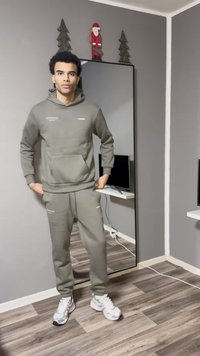 Sweatshirt cinzento e joggers combinando, ambos com textura suave. O conjunto apresenta um bolso frontal e detalhes discretos com o logotipo. Tênis brancos completam o visual.