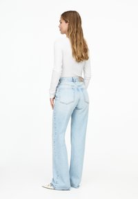 Jeansi de culoare bleu deschis, cu talie înaltă și croială relaxată, având două buzunare posterioare și o etichetă vizibilă la talie. Textură netedă de denim.