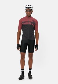 Maillot de cyclisme à manches courtes en bordeaux et noir avec des rayures géométriques, associé à un short noir, des chaussures de cyclisme, des gants et un casque blanc.
