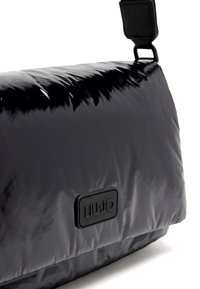 Borsa a tracolla nera, lucida e sintetica con una texture liscia e imbottita; presenta una forma rettangolare e una patch del logo testurizzata sulla parte frontale.
