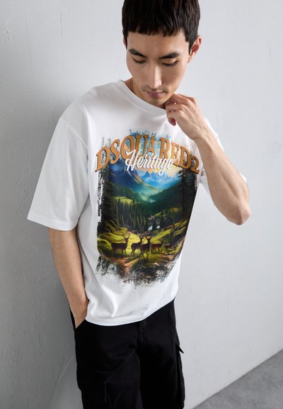 Hvid t-shirt med et farverigt grafisk motiv, der viser en skovscene med hjorte; indeholder teksten "DSQUARED2" og "Heritage" i kontrastfarver.
