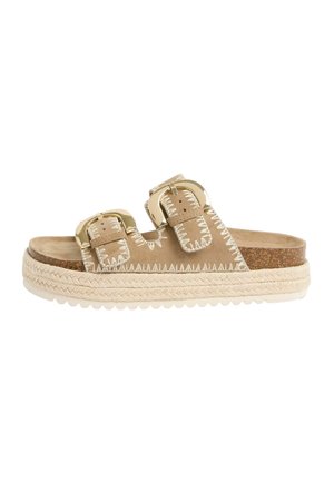 Beige slide sandal with two large gold buckles, white stitching, braided rope platform sole, and cushioned cork footbed.
