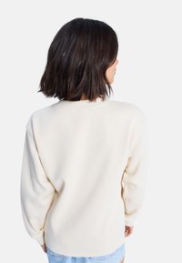 Sudadera color crema con un corte relajado, cuello redondo y mangas largas. Textura suave; sin patrones ni acentos visibles.