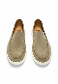 Beige mokasiner lavet af ruskind med en glat overflade, rund tå og hvid gummisål. Branding synlig på den indre sål.