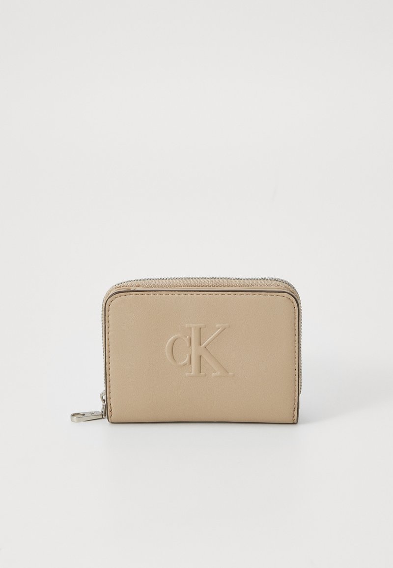 Portafoglio in pelle beige con logo "CK" in rilievo, chiusura a zip, forma rettangolare e texture liscia. Design compatto con dettagli minimi.