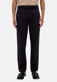 Marineblaue Leinenhose mit entspannter Passform, ausgestattet mit Falten, einem Knopfverschluss und schmal zulaufenden Knöcheln. Tragen Sie dazu schwarze Slipper.