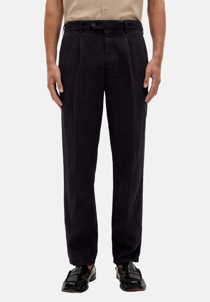 Marineblaue Leinenhose mit entspannter Passform, ausgestattet mit Falten, einem Knopfverschluss und schmal zulaufenden Knöcheln. Tragen Sie dazu schwarze Slipper.