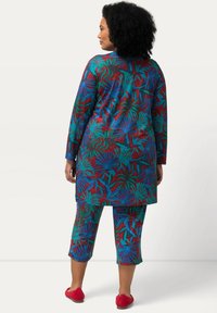 Ensemble de salon coloré comprenant une longue tunique et un pantalon capri. Fabriqué en tissu doux avec un motif de feuilles vif en rouge, vert et bleu. Chaussures rouges.